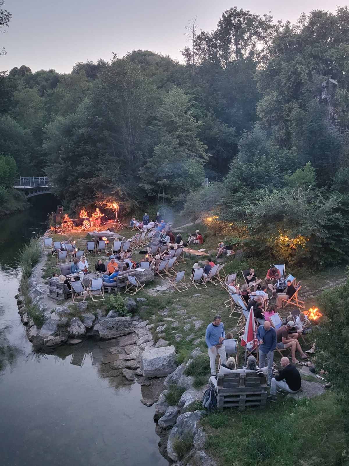 Abendstimmung mit Lagerfeuer und Gästen auf den Steinen am Fluss