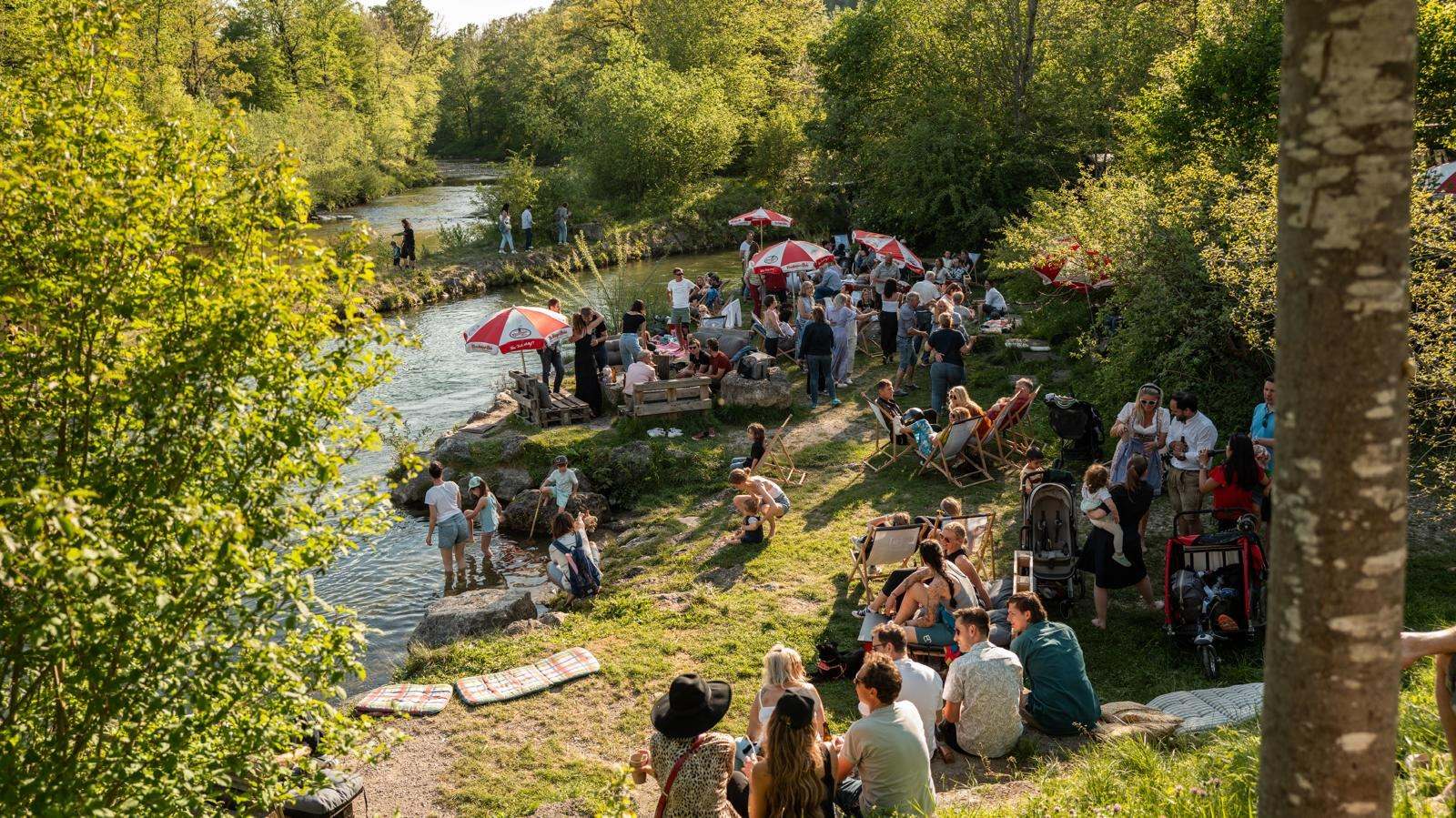 Panorama vom Traunufer: viele Gäste auf der Wiese und am Wasser unter Sonnenschirmen